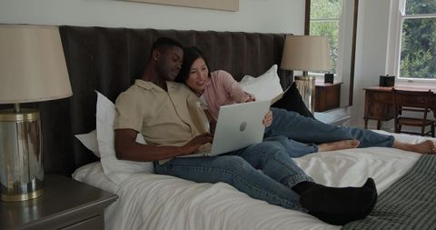 Couple relaxing in bed shopping online together with laptop
