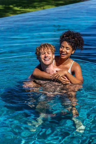 Couple laughing and embracing in infinity pool on sunny day for summer romance and travel