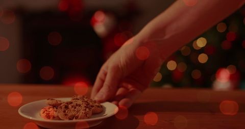 Hand Placing Cookies on Plate Amid Festive Christmas Lights - Download Free Stock Images Pikwizard.com