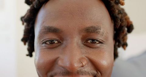 Smiling black man closeup headshot with nose hoop and twisted locs, soft natural light
