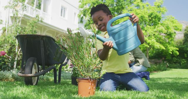 Young boy watering potted plant in garden during sunny day, surrounded by lush greenery and a wheelbarrow. Ideal for themes related to childhood, gardening, outdoor activities, environmental awareness, or family bonding.