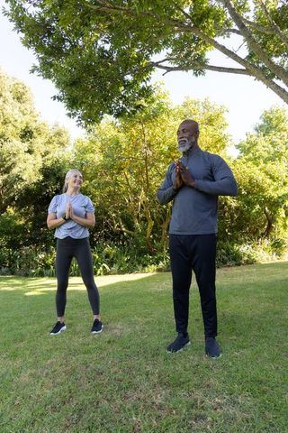 Diverse adults practicing outdoor yoga on lawn standing in prayer pose wearing activewear