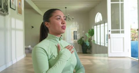 Woman practicing mindful breathing in sunlit foyer with arched windows and plants