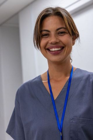 Smiling female clinician wearing grey scrubs and blue lanyard standing in clinic corridor