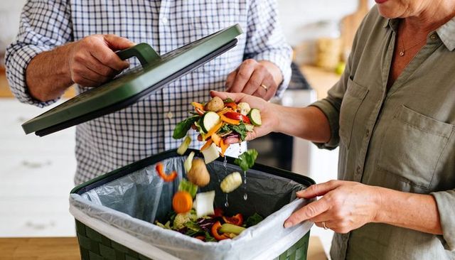 Couple composting vegetable scraps into green kitchen bin promoting sustainable home waste