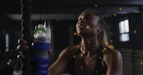 Female athlete gripping rope and holding hydration bottle amid gold star confetti
