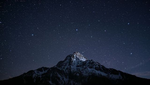 Solitary snow-capped peak rising beneath vast starfield, alpine night wilderness
