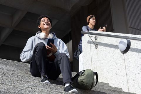 Smiling college student relaxing on campus steps using smartphone while holding football