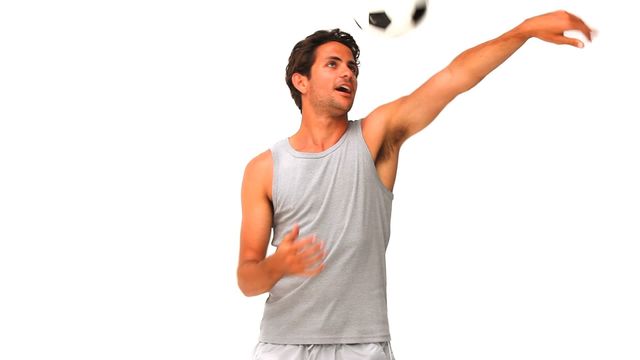 Young man energetically throwing a soccer ball while wearing casual sportswear against a white background. Ideal for use in sports and exercise promotions, athletic gear advertisements, or any campaign emphasizing energetic activities.