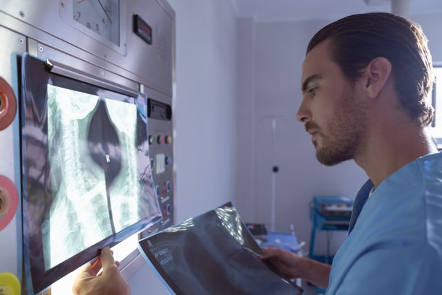 This image depicts a male surgeon wearing scrubs, closely examining an x-ray on a light box in a hospital operation room. This photo could be used for medical and healthcare-related content, such as articles on surgical procedures, medical diagnosis, radiology, hospital environments, or professional medical training materials.