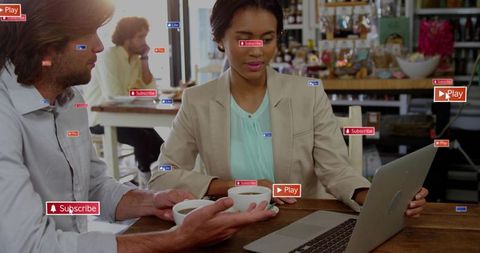 Businesswoman collaborating over laptop in cafe while colleague offering coffee