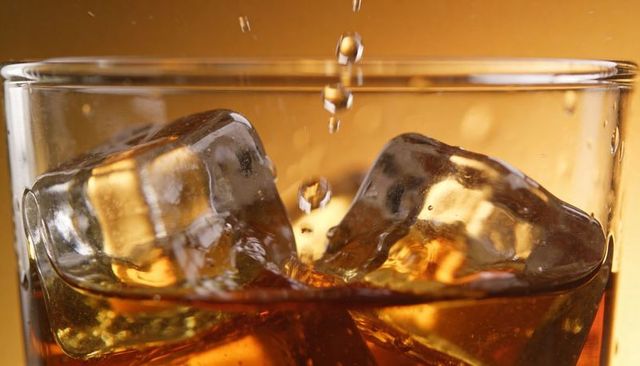 Whiskey splashing over ice with golden droplets, warm backlight macro closeup