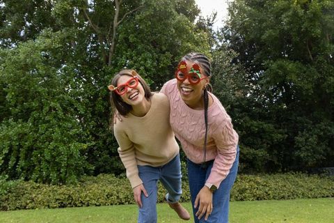 Friends laughing in garden wearing festive novelty glasses and cozy knit sweaters