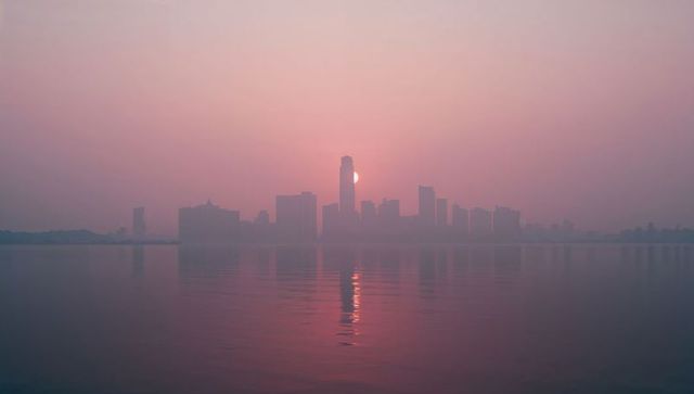 Silhouette of Urban Sunrise with Pastel Hues Reflecting Over Water