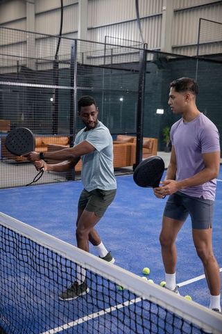 Indoor padel training duo practicing volleys on blue court with modern black paddles