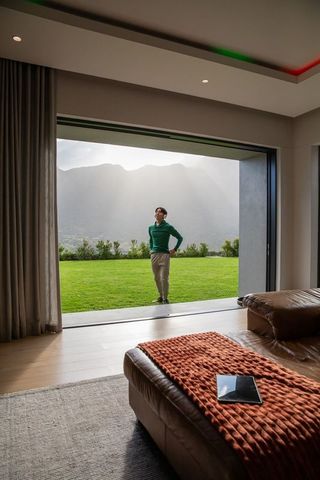 Asian man standing at open sliding door overlooking mountain lawn, modern living room