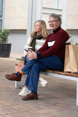 Senior couple relaxing on urban bench with coffee and shopping bags, smiling together