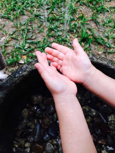 Child’s hands catching raindrops in an outdoor area with grass and small stones. Could be used for themes such as nature, childhood experiences, fresh water, environmental conservation, rainwater harvesting, innocence, and outdoor activities.