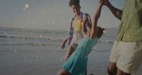 Family walking on beach holding hands and swinging child by ocean waves at golden hour