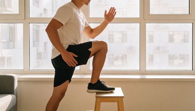 Man stepping onto stool for home workout balancing in sunlit apartment living room