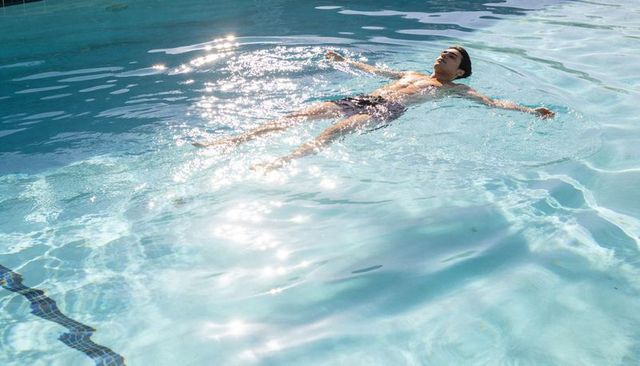 Man floating calmly in sunlit turquoise pool with glinting reflections
