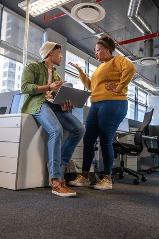 Diverse Coworkers Arguing in Open-Plan Office Using Laptop and Smartphone, Tense Discussion
