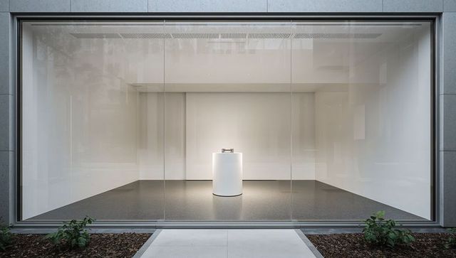 Minimalist storefront gallery featuring white cylindrical pedestal and reflective glass