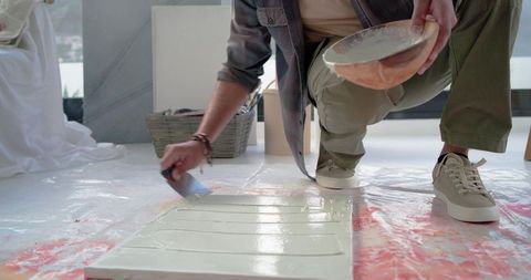Indian man kneeling smoothing plaster on panel with putty knife in bright studio workspace
