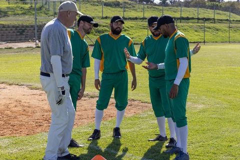 Baseball team huddling with coach on sunny practice field discussing strategy