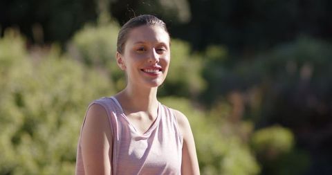 African american woman smiling in sunlit garden wearing pastel pink sleeveless top