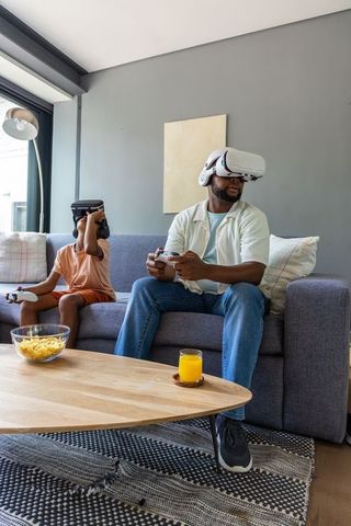 African american father and teenage son playing vr together on living room couch