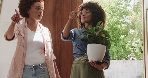 African American Friends Standing Pointing and Holding Houseplant in Sunny Entryway