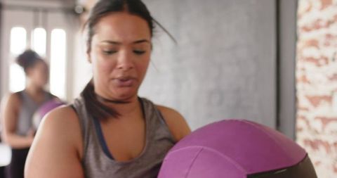 Two women training with purple medicine balls in bright urban gym for partner workout