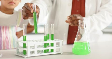 African American woman mentoring child in chemistry experiment with green liquid