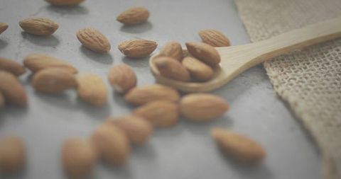 Wooden Spoon Holding Whole Almonds on Rustic Stone Slab with Burlap Texture, Closeup
