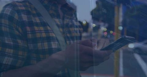 Mid-adult man tapping smartphone on city sidewalk at night with bokeh reflections