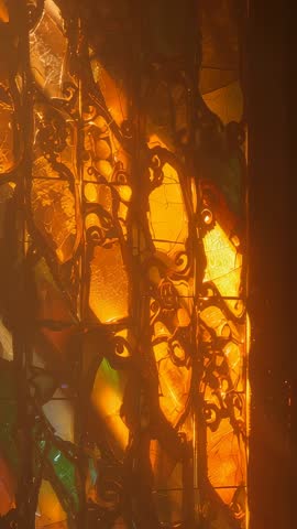 Sunlight Streaming through Stained Glass and Ornate Grille Casting Moving Amber Shadows