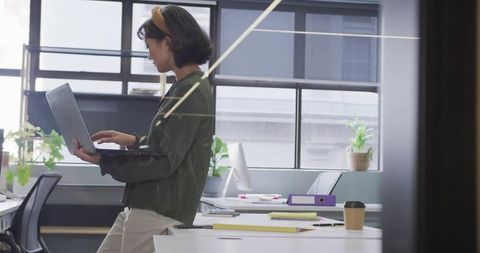 Young professional working on laptop in bright modern office with plants and coffee cup