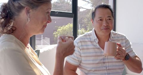 Diverse couple relaxing together with warm drinks in cozy living room