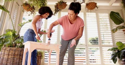 Mother and Daughter Painting Wooden Table Together in Sunlit Room