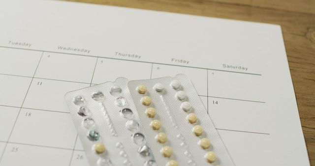 Blister pack of birth control pills placed over a calendar highlighting routine medication use. Suitable for articles on family planning, women's healthcare, and reminders for taking medication regularly.