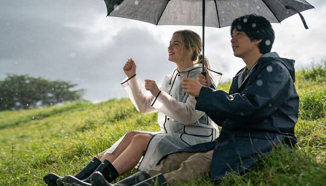 Couple sitting on grassy hillside sharing umbrella in rain, smiling and enjoying moment