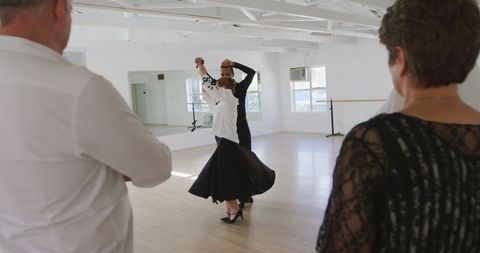 Mature woman and instructor ballroom dancing with friends observing