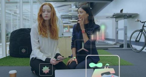 Two businesswomen collaborating with ar overlays in modern coworking space using laptop