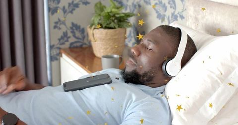 Relaxing man listening to music with headphones while reclining on bed with smartphone
