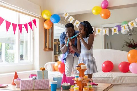 African american father and daughter blowing party blowers at home birthday celebration