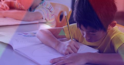 Elementary boy writing in workbook holding pencil concentrating on learning and drawing