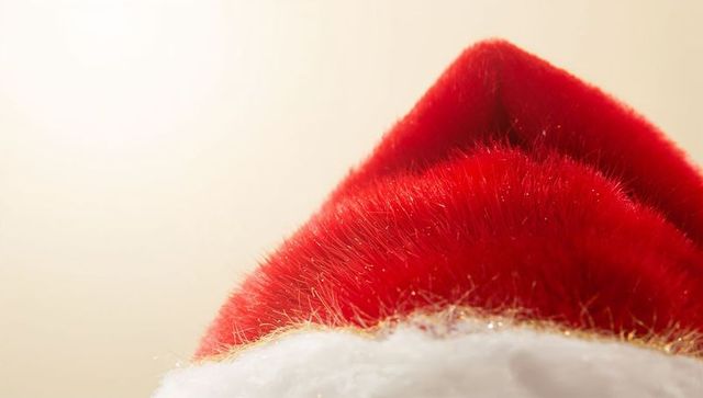Classic red santa hat closeup with sparkling white fur trim on soft beige background