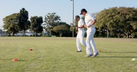Timing agility drill as two athletes perform cone shuttle runs on mowed grass field