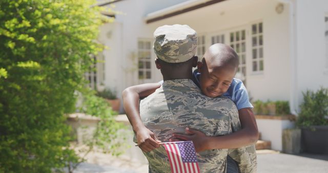 Happy african american male soldier and his son embracing outside the house. Military, patriotism, family, and togetherness.